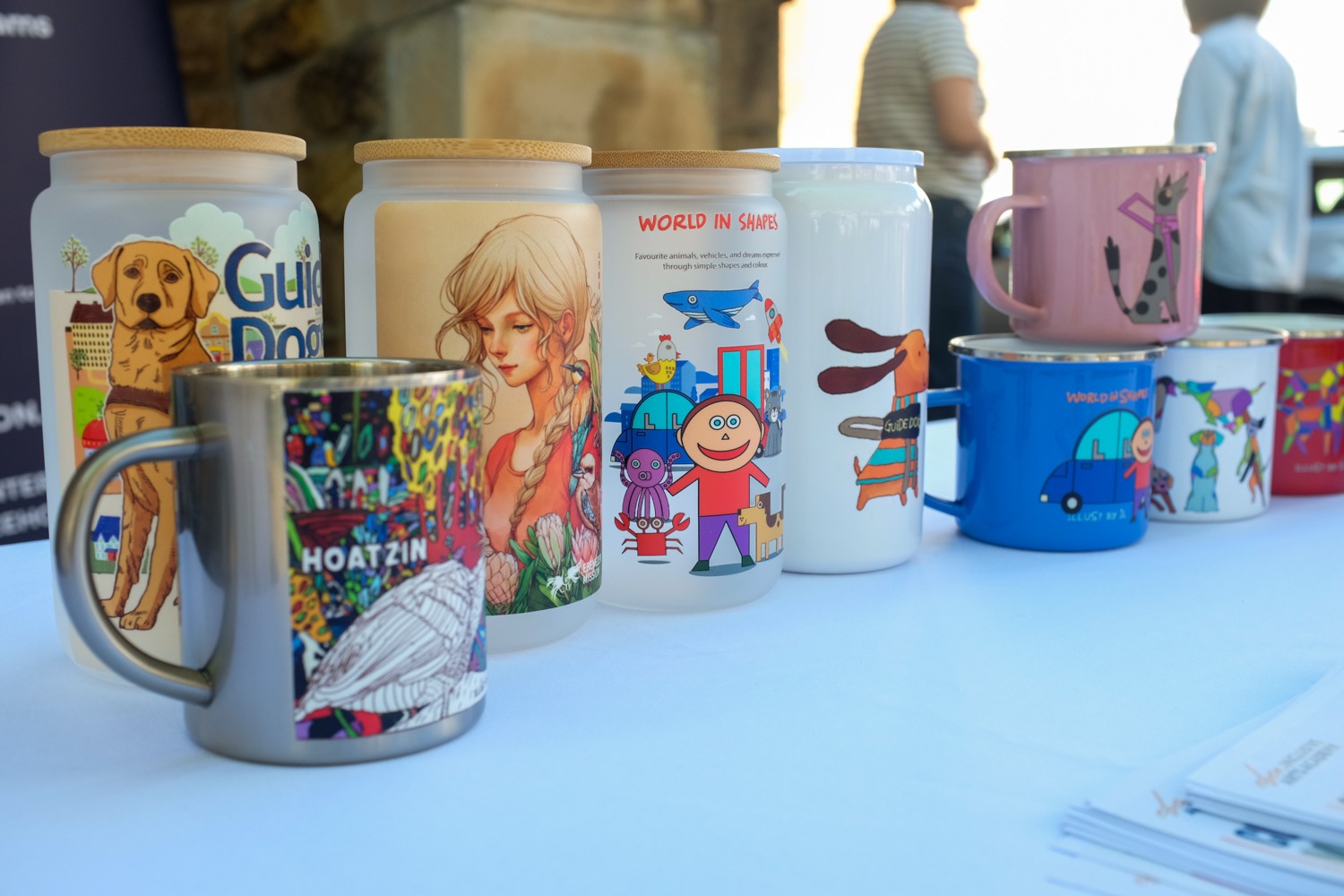 A collection of mugs and tumblers featuring original designs by artists with disability